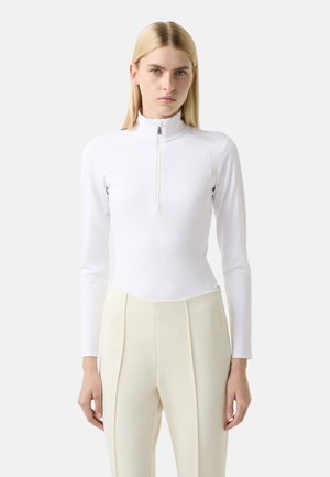 Witte lange mouwen top met een halve ritssluiting en een gladde textuur, gecombineerd met crèmekleurige hoge taillebroek met verticale plooien.