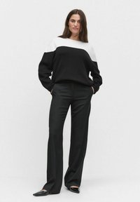 Zwart-wit blokken trui en zwarte op maat gemaakte broek. De trui heeft een relaxte pasvorm met een color-block ontwerp. Soepele textuur, lange mouwen.