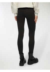 Czarne legginsy o gładkiej fakturze, wysokim stanie i dopasowanym kroju, zestawione z czarnymi, masywnymi botkami na kostkę z grubą podeszwą.