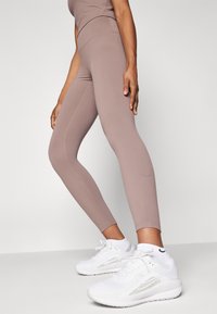 Bruine, aansluitende legging met een gladde textuur en zijnaad, gecombineerd met witte sportschoenen met een zilveren accent en een gestructureerd ontwerp.