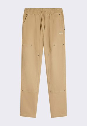 Beige cargobroek met een elastic waistband, trekkoord en meerdere zakken. Voorzien van metalen drukkers en stikselaccenten.