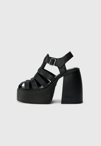 Black platform sandals with wide crossed straps, adjustable ankle strap, and chunky heel. Made of smooth material with minimal detailing.