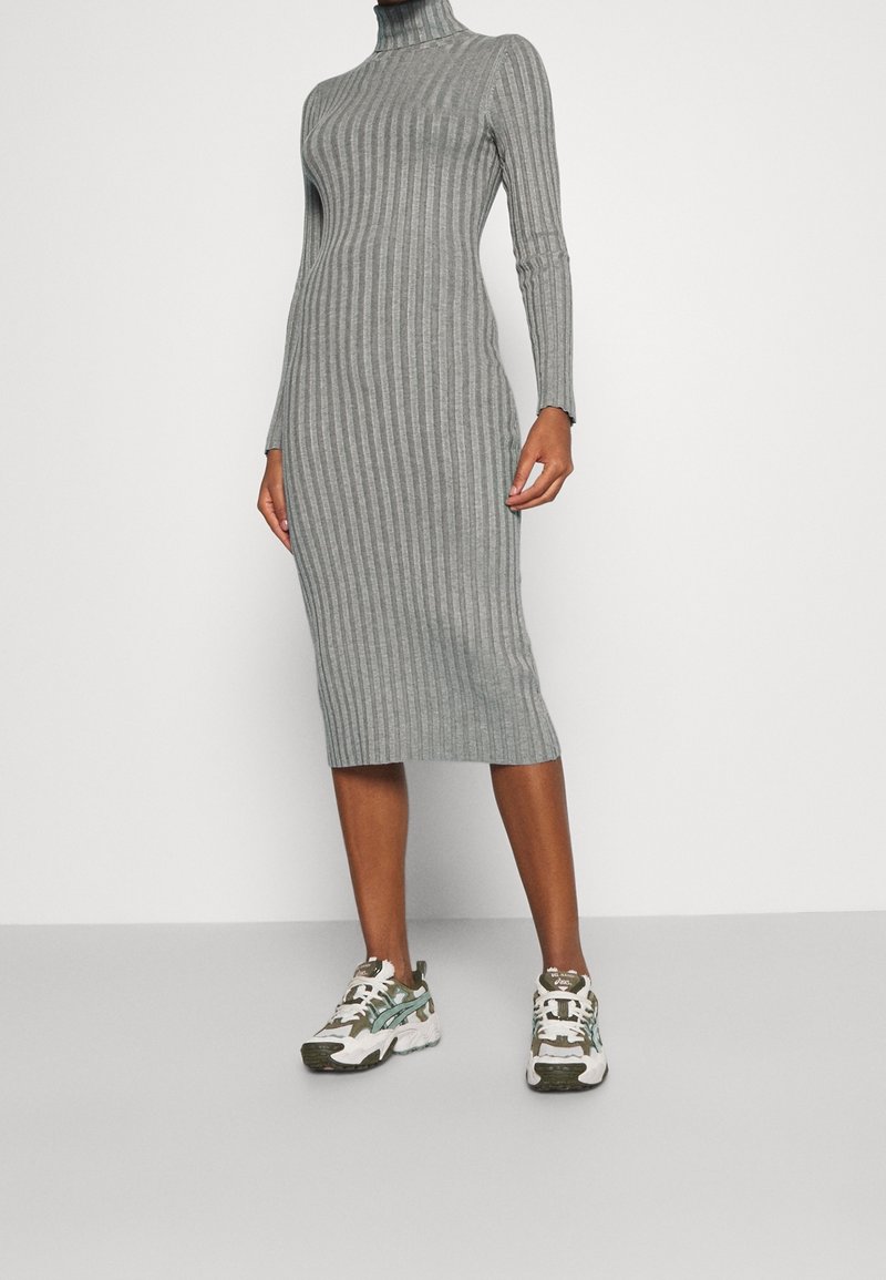 Robe midi gris côtelée avec un col montant et des manches longues, associée à des baskets blanches et vertes à motifs. Texture lisse, silhouette ajustée.