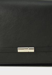 Borsa nera in pelle con una texture liscia, dotata di una chiusura con accento dorato e dettagli cuciti. Forma rettangolare compatta.