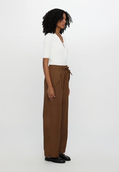 White fitted top with a collar, paired with brown wide-leg trousers featuring a drawstring waist and large side pockets. Black shoes.