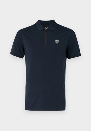 Polo de color navy con mangas cortas, cuello con cremallera y un pequeño logo bordado en el pecho. Tela suave y ligera.
