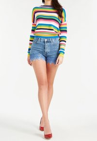Suéter de manga larga a rayas en colores vibrantes, combinado con shorts de denim azul con un dobladillo de encaje con volante. Zapatos de tacón rojos completan el atuendo.