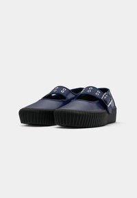 Marineblauwe rubber instappers met zwarte dikke ribbelzolen en verstelbare banden met metalen oogjes en gespen.