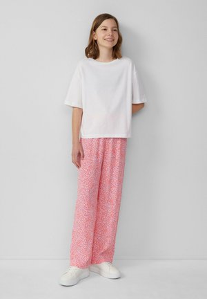 White cotton T-shirt with short sleeves paired with pink patterned loose pants. Simple white sneakers complete the outfit.