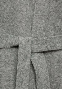 Accappatoio grigio realizzato in un morbido tessuto testurizzato con cintura coordinata. La vista ravvicinata mostra i dettagli della superficie del tessuto e la tessitura.