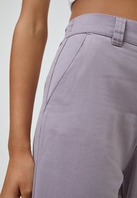 Pantalons lilas en tissu léger, avec une texture lisse, une coupe ajustée et un design épuré agrémenté de détails subtils sur les coutures latérales.