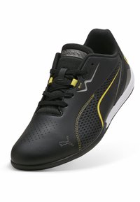 Schwarzer Sportschuh mit perforiertem Obermaterial, gelben Akzenten und strukturierten Schnürsenkeln. Verfügt über ein schlankes Design und eine kontrastierende weiße Sohle.