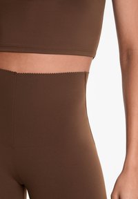 Barna cropped top és magas derekú leggingsek, sima, rugalmas anyagból. Mindkét ruhadarab szegélyén fodros rész található.