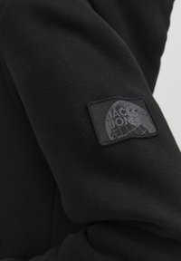 Felpa nera con una texture morbida, dotata di un'etichetta rettangolare nera sul manica che mostra il logo "Jack & Jones" in un design tonale.