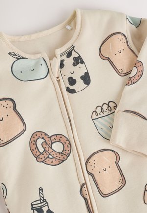 Combinaison beige à fermeture éclair ornée d'illustrations sur le thème de la nourriture : pain, bretzels et lait. Matière en coton doux avec poignets côtelés.