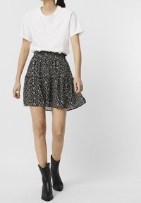 T-shirt bianco a maniche corte abbinato a una gonna floreale nera con orlo arricciato, indossata con stivaletti alla caviglia neri con texture.