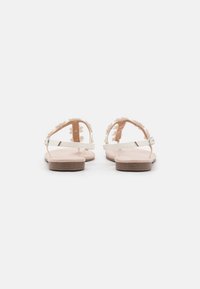 White flower-adorned sandals with a flat, light wood sole and thin ankle strap. Soft pink base with floral accents around the foot.