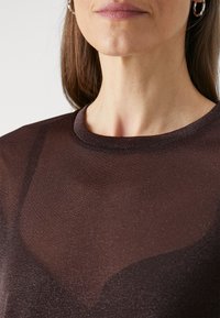 Sötétbarna, félátlátszó felső, kerek nyakkal. Az anyagnak finom fényessége van; sima tapintású és testhezálló fazonú.