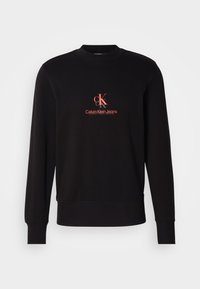 Černá mikina s žebrovaným kulatým výstřihem, dlouhými rukávy a výrazným červeným logem "CK" s nápisem "Calvin Klein Jeans" na přední straně.