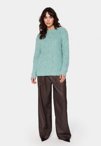 Mėtų žalios spalvos mezgimas su laisvu siluetu, raukšlėtomis rankovėmis ir apačia, derinamas su tamsiai rudos spalvos plačiomis kelnėmis.