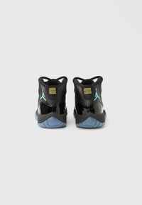 Ζευγάρι μαύρα ψηλά αθλητικά παπούτσια με γυαλιστερές λεπτομέρειες, παγωμένους μπλε πάτους, λογότυπο Jumpman σε τιρκουάζ και κίτρινη ριγωτή λεπτομέρεια στη φτέρνα.