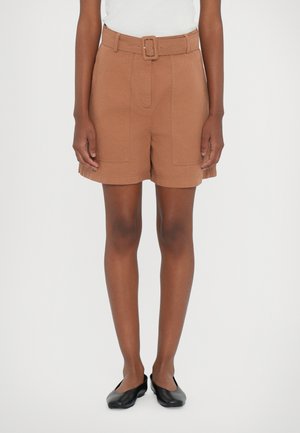 Bruine short met ceintuur en een op maat gemaakte snit, voorzien van steekzakken en een gestructureerde stof, gecombineerd met zwarte platte schoenen.