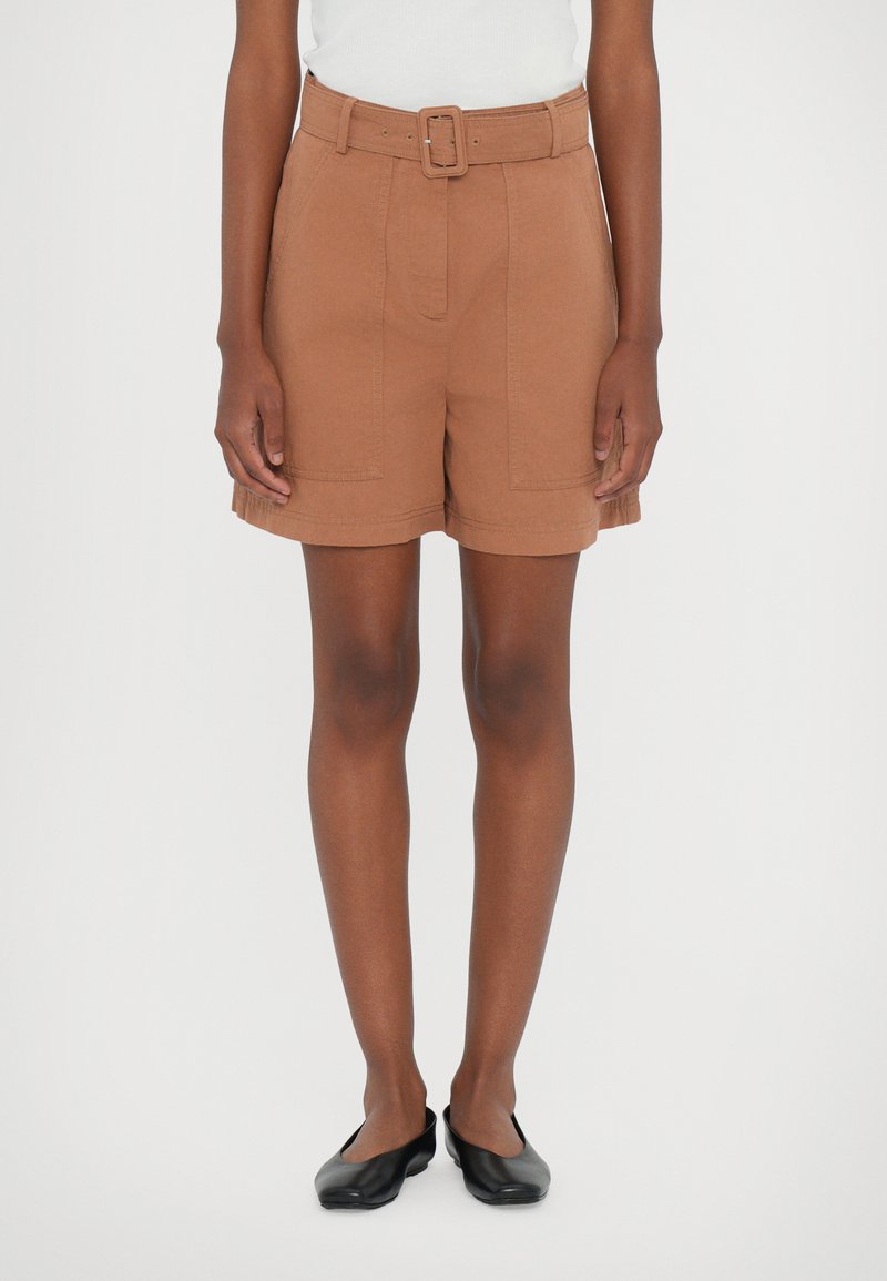 Shorts marron à ceinture, avec un design sur mesure, comportant des poches avant et un tissu texturé, associés à des chaussures plates noires.