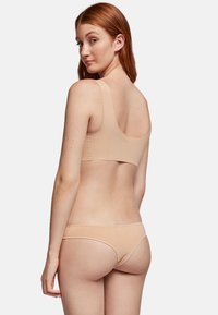 Conjunto de sujetador y bikini en tono nude, que presenta una textura suave, tirantes anchos y un diseño minimalista con detalles de banda elástica.