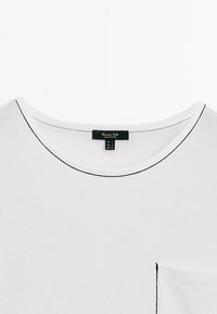 T-shirt blanc col rond avec surpiqûres noires autour de l'encolure et de la poche, affichant l'étiquette de la marque au col.