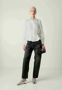White, long-sleeve shirt with peplum waist, paired with black high-waisted jeans. Accessories include a small black bag and silver shoes.