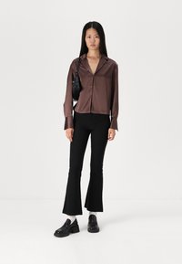 Brown satin collared blouse with a button front and long sleeves, paired with black flared pants and chunky black shoes. Small black bag.