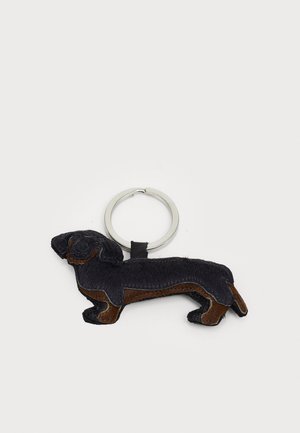 Leren sleutelhanger in de vorm van een hond met zwarte en bruine kleuren, een gestructureerd vachtachtig oppervlak en een zilveren ring om de sleutels aan te bevestigen.