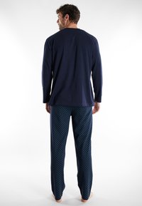 Marineblaues Langarmoberteil mit Rundhalsausschnitt, kombiniert mit gemusterten Hosen mit kleinen blauen Punkten auf dunklem Hintergrund; aus Baumwollmaterial.