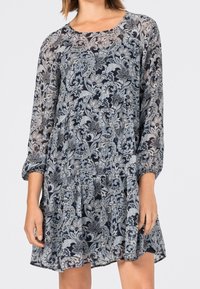 Pitkähihaisen mekko tummansinisen ja vaaleanharmaan kukkakuosin kanssa, jossa on kerätty vyötärö ja virtaava kangas kerrosvaikutuksen luomiseksi.