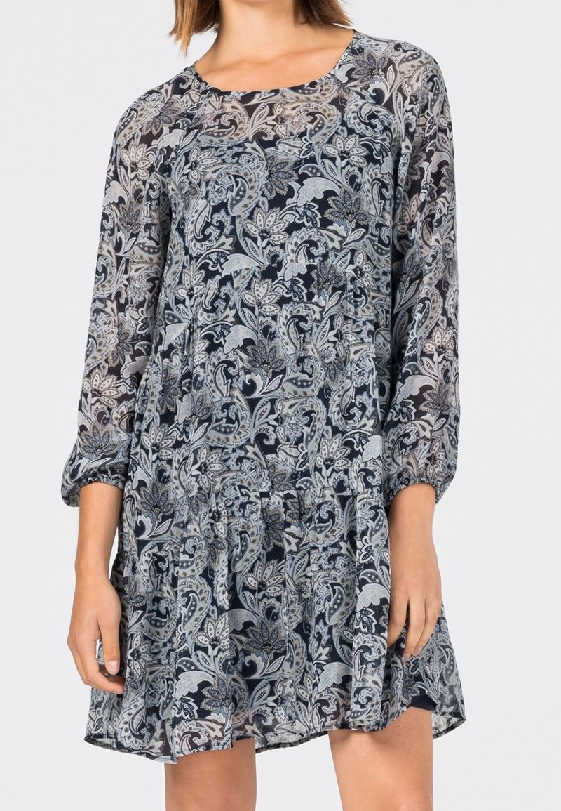 Pitkähihaisen mekko tummansinisen ja vaaleanharmaan kukkakuosin kanssa, jossa on kerätty vyötärö ja virtaava kangas kerrosvaikutuksen luomiseksi.