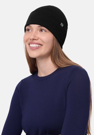 Black knit beanie with a smooth texture and folded cuff. Features small logo tag. Worn with a navy long-sleeve shirt.