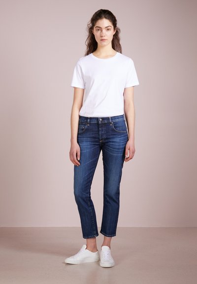 Witte t-shirt, donkerblauwe jeans en witte sneakers. De jeans zijn slimfit met een lichte taper en subtiele vervaging. Minimalistisch ontwerp.