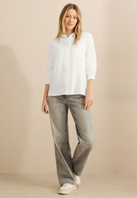 Hvid tekstureret skjorte med krave, parret med grå brede bukser og hvide sneakers; minimalistisk design, afslappet pasform.