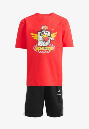 T-shirt rouge à manches courtes avec un graphique de joueur de basketball en dessin animé et des accents jaunes, associé à un short noir avec des bandes blanches sur les côtés et un logo.