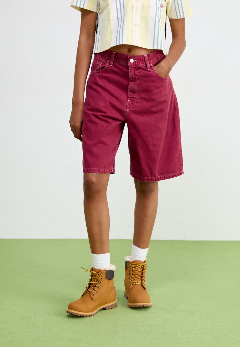 Shorts in denim borgogna con una vestibilità morbida, tasche frontali e chiusura a bottone, abbinati a stivali in tan con lacci e colletto morbido.