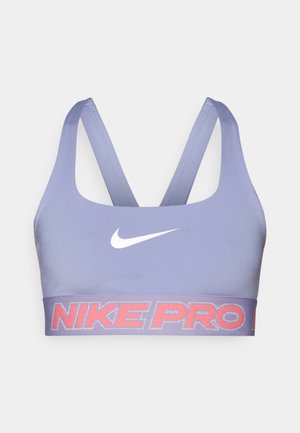Nike Pro sports-bh i lys lilla med ensartet tekstur, med en hvid Nike-logo og et kontrasterende rødt logo-bånd nederst.
