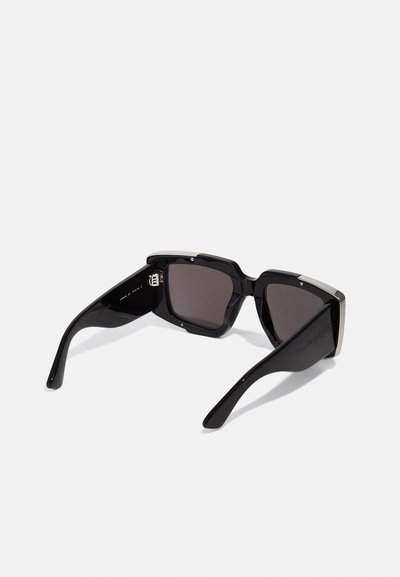 Ochelari de soare supradimensionați cu rame din plastic negru și lentile întunecate, având accente metalice în partea de sus. Brațele texturate oferă o prindere bună.