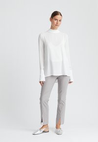 Witte blouse met lange mouwen en een hoge hals, gecombineerd met lichtgrijze slim-fit broek met zijsplits en metallic slingback schoenen.