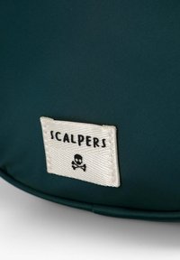 Bolsa de tela verde con una etiqueta crema que dice "SCALPERS" y un gráfico de calavera y huesos cruzados, destacando su distintiva marca y textura.
