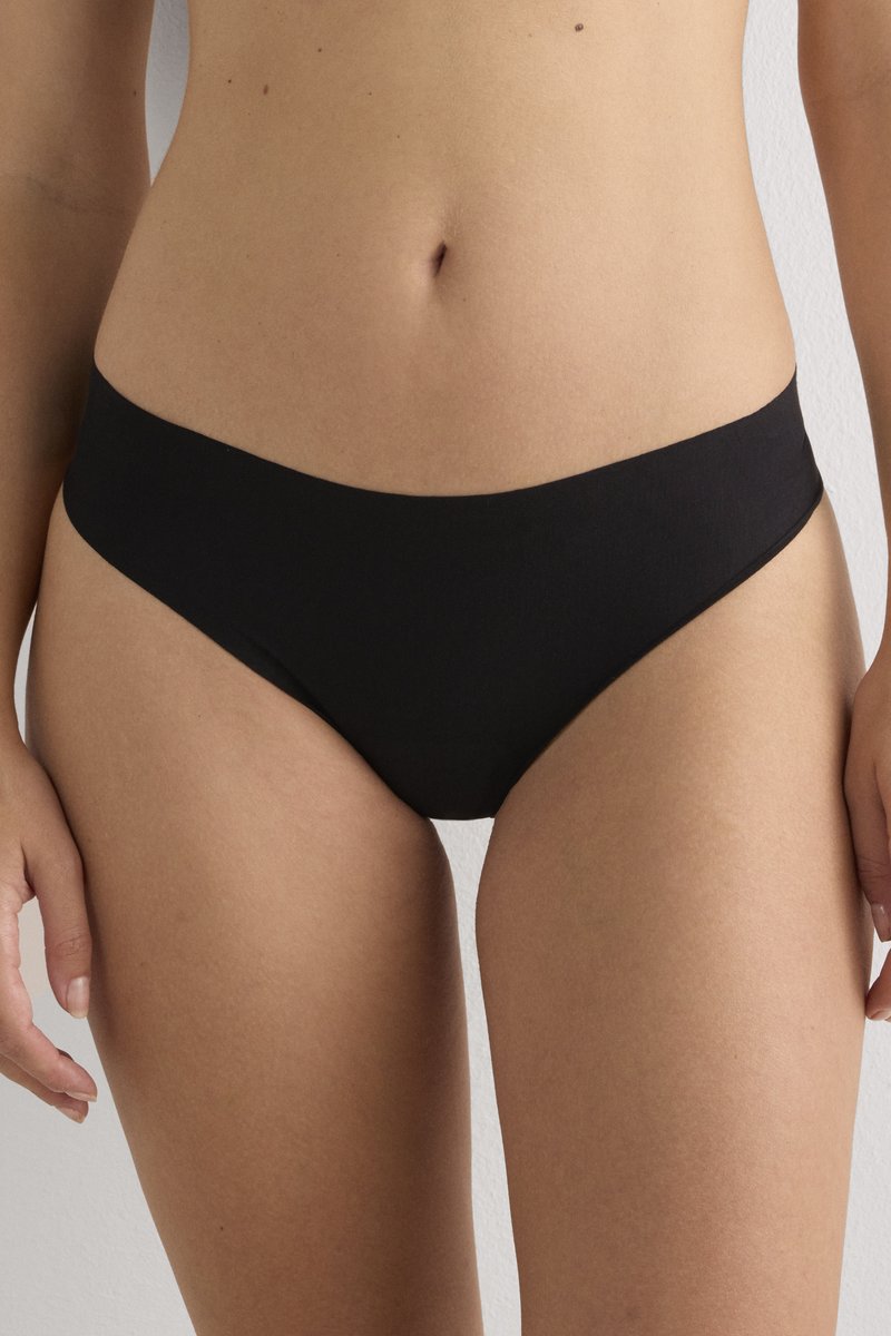 Vrouw draagt eenvoudige zwarte bikini-onderbroek met lage taille, zichtbaar van midden torso tot bovenbenen tegen een neutrale achtergrond.