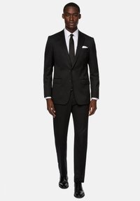 Černý oblek s jednobreasted sako a klopovými límci. Bílá košile s límcem a černá kravata. Černé společenské boty. Přizpůsobený střih.