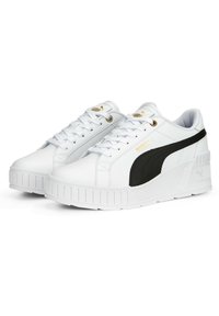 White sneakers with a black side stripe, made of synthetic material. Features flat laces, a thick sole, and gold accent branding.