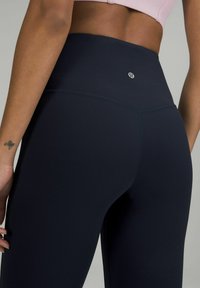 Legginsy w kolorze granatowym z wysokim stanem, wykonane z gładkiego, elastycznego materiału, z logo z tyłu i płaskimi szwami dla komfortu.