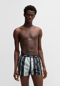 Boxershorts med sorte og lyseblå lodrette striber, en sort elastik med "HUGO"-logo og en knapdetalje foran.