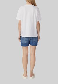 T-shirt en coton blanc à manches courtes, associé à un short en denim bleu avec des bords effilochés, et des chaussures à plateforme blanches, vu de l'arrière.